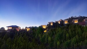 A row of modern, multi-story buildings with large windows, situated on a hillside with dense forest. - Grand Bay Hotel Beijing (Miyun)