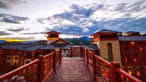 A wooden bridge leading to a building with multiple red railings and a mountainous backdrop. - Grand Bay Hotel Beijing (Miyun)