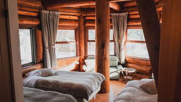 A log cabin room with two beds, a small table, and a chair.