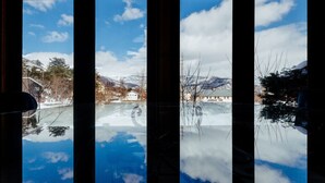 A view through a window with a reflection of a snowy landscape, including mountains and buildings. - Hakuba Log Hotel Meteor (Hakuba)