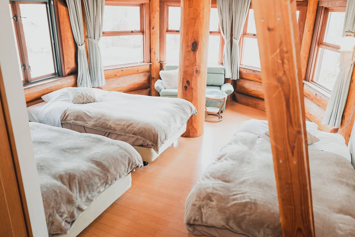 A cabin with three beds, wooden floors, and large windows.