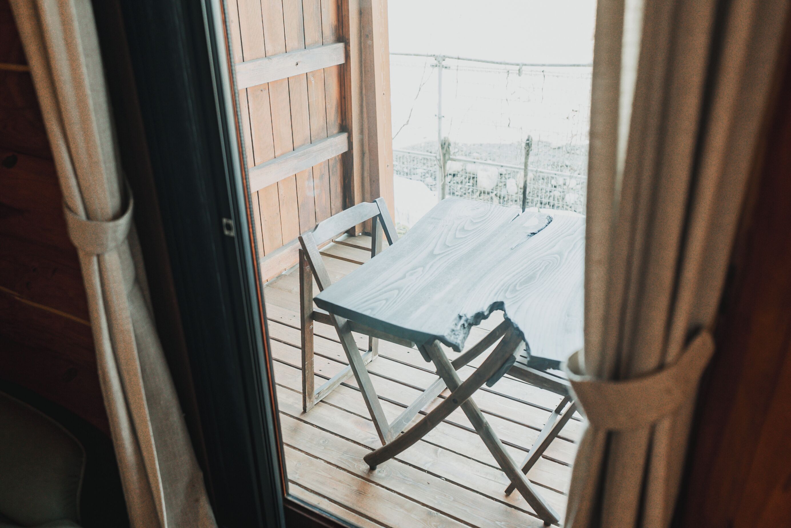 Une terrasse en bois avec une table et des chaises, un mur en bois et une vue sur un paysage enneigé.