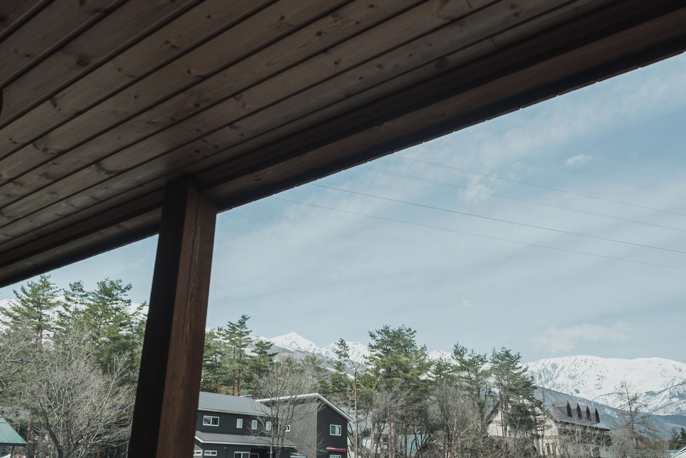 A view from a covered area with a wooden ceiling, looking out at a mountain range and buildings in the background.