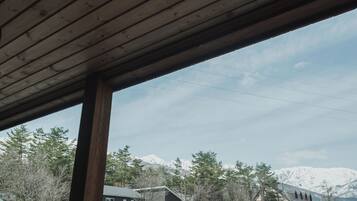 A view from a covered area with a wooden ceiling, looking out at a mountain range and buildings in the background.