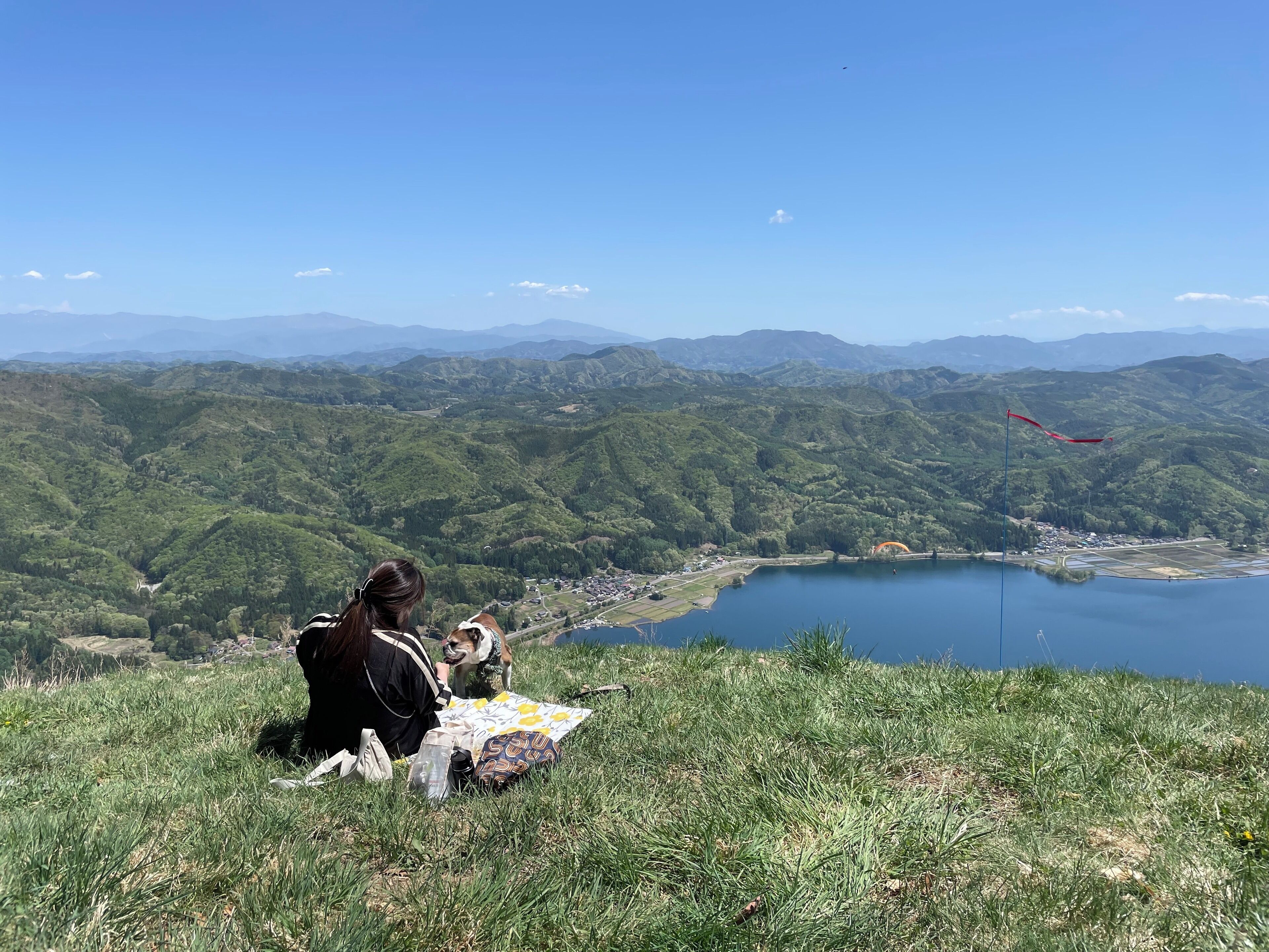 Une personne assise sur une colline herbeuse, d’où l’on a une vue sur un lac et des montagnes.