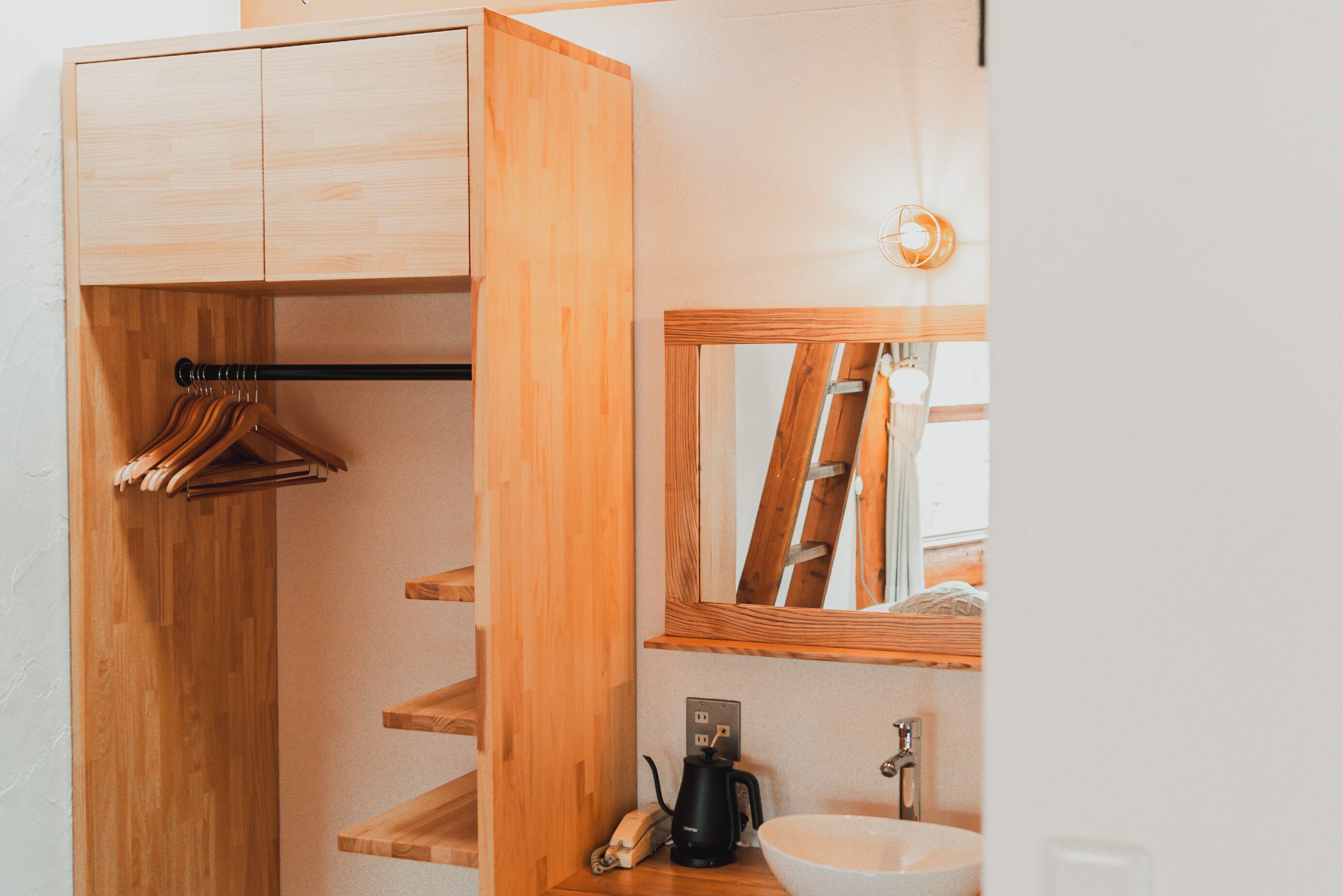 A wooden wardrobe with hanging space, a mirror, a sink, and a coffee maker.