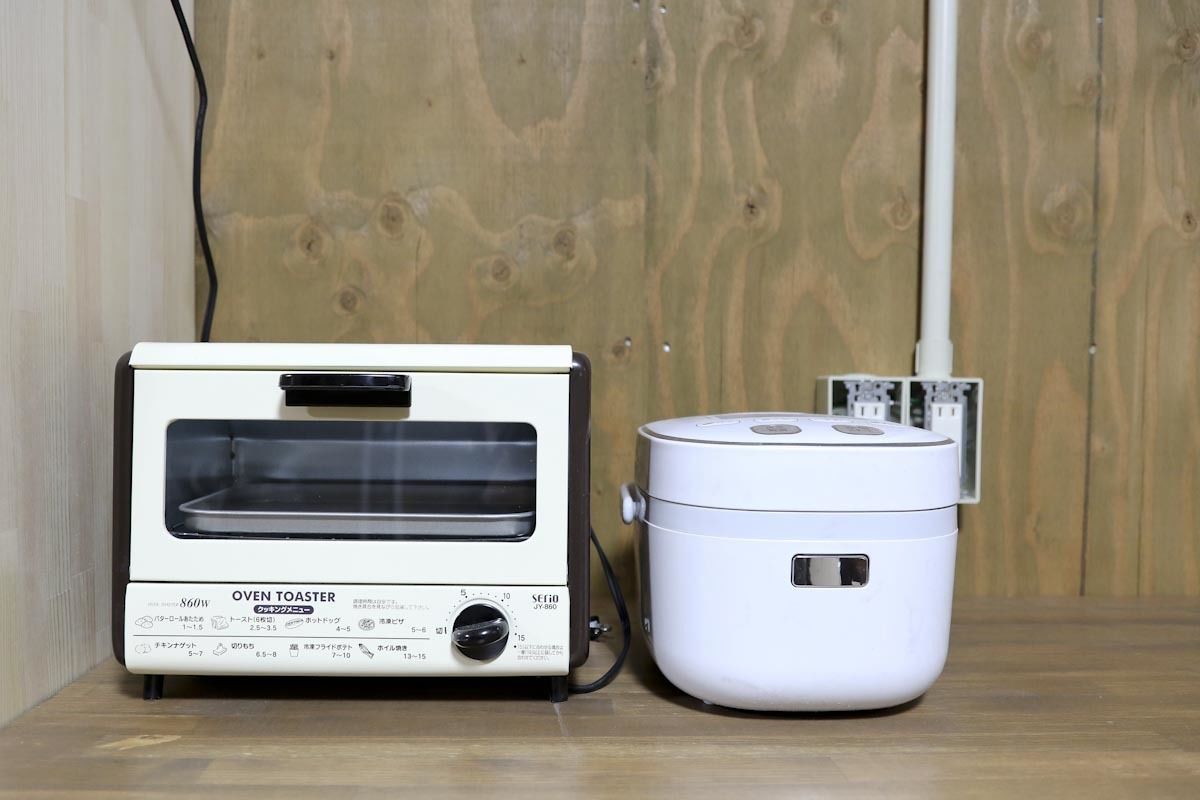 An oven toaster and a rice cooker on a wooden surface.