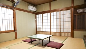 A tatami mat room with a low table and cushions, wooden sliding doors, and an air conditioning unit. - Guest House Route53 Furuichi (Nara)