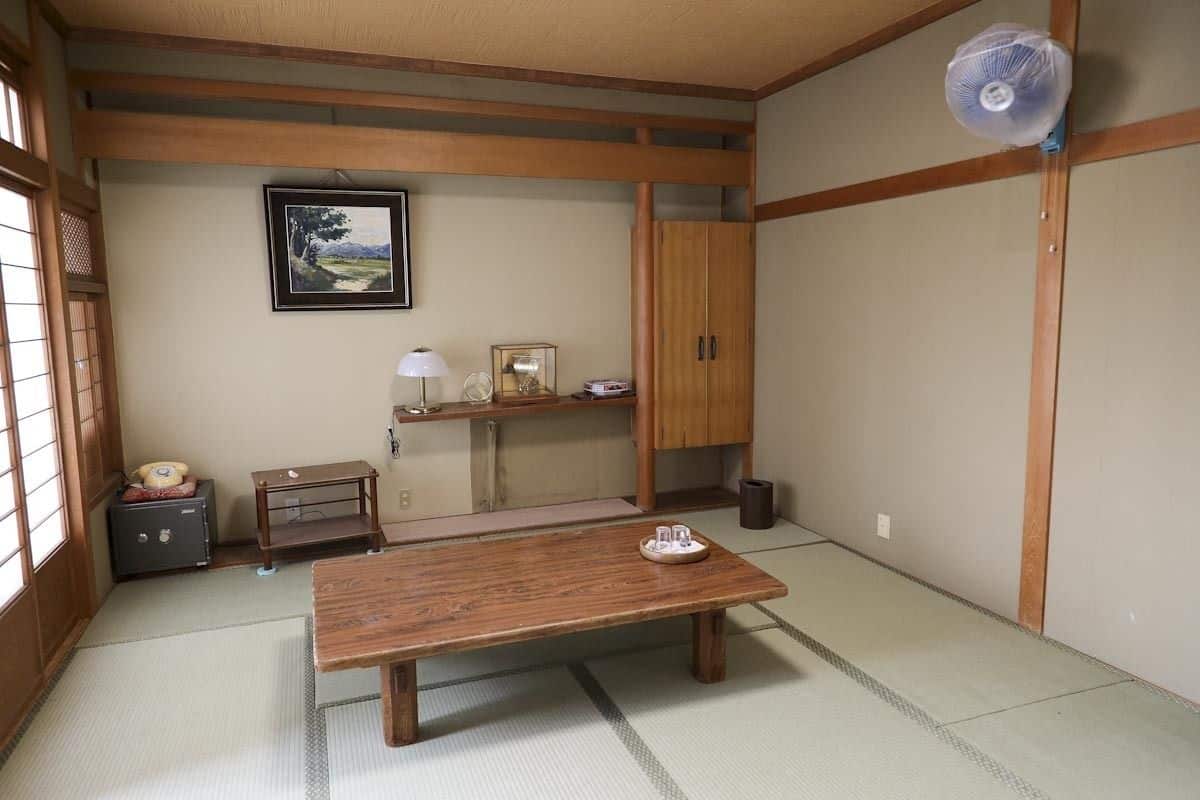 A traditional Japanese room with tatami flooring, a wooden table, a cabinet, a fan, and a framed picture on the wall.