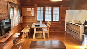 Un interior de cabaña acogedor con una mesa de comedor de madera, sillas, un televisor y una zona de cocina.