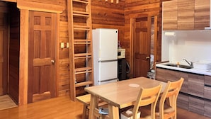 Interior de una cabaña de madera con comedor, cocina y habitación superior con escalera.