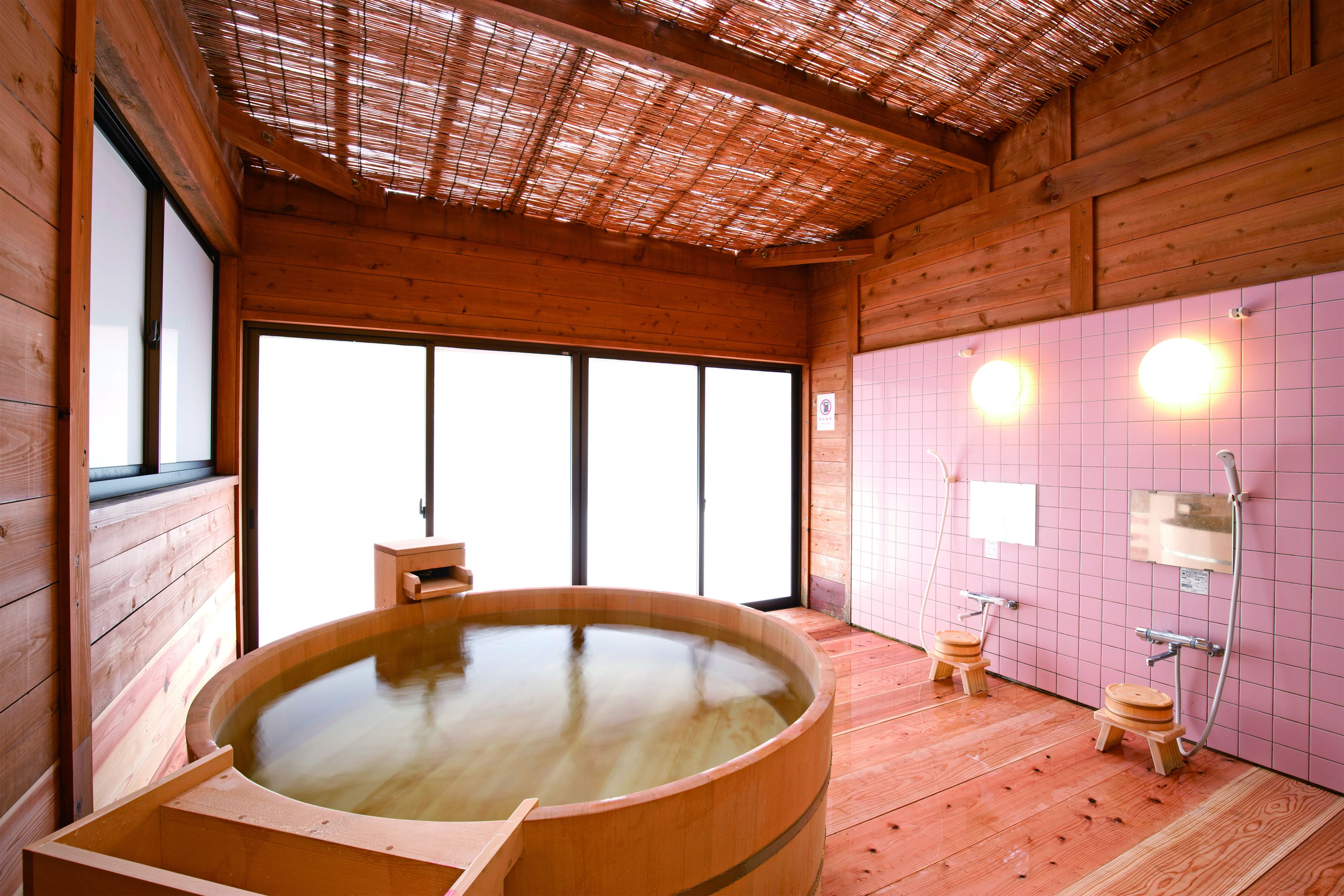 Un cuarto de spa de madera con una amplia bañera de madera, dos taburetes de madera y un muro con azulejos que incluye una zona de ducha.