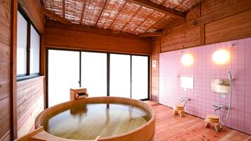 Un cuarto de spa de madera con una amplia bañera de madera, dos taburetes de madera y un muro con azulejos que incluye una zona de ducha.