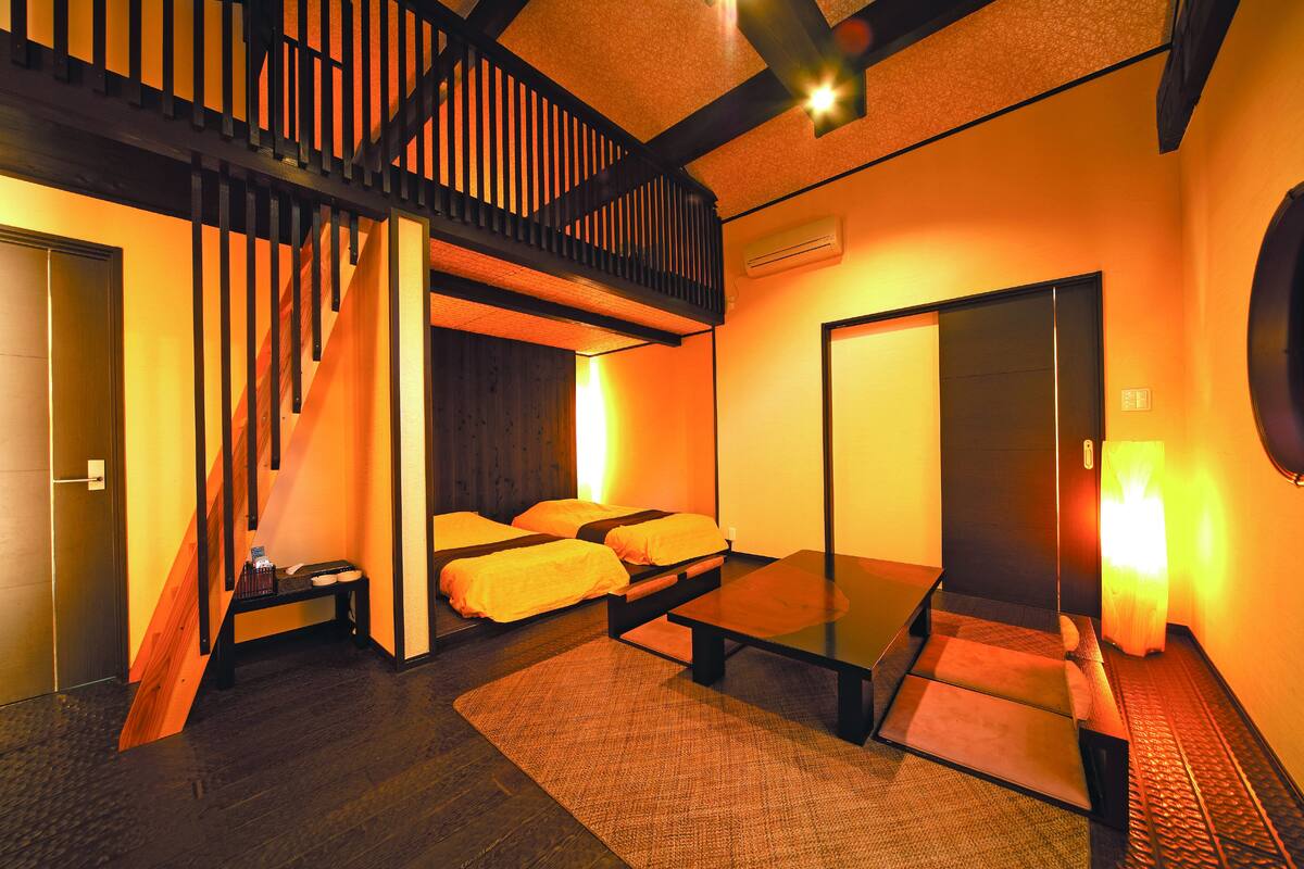 Ein Hotelzimmer mit einer Holztreppe, einem Bett mit orangefarbener Bettwäsche, einem kleinen Tisch und einer Bank.