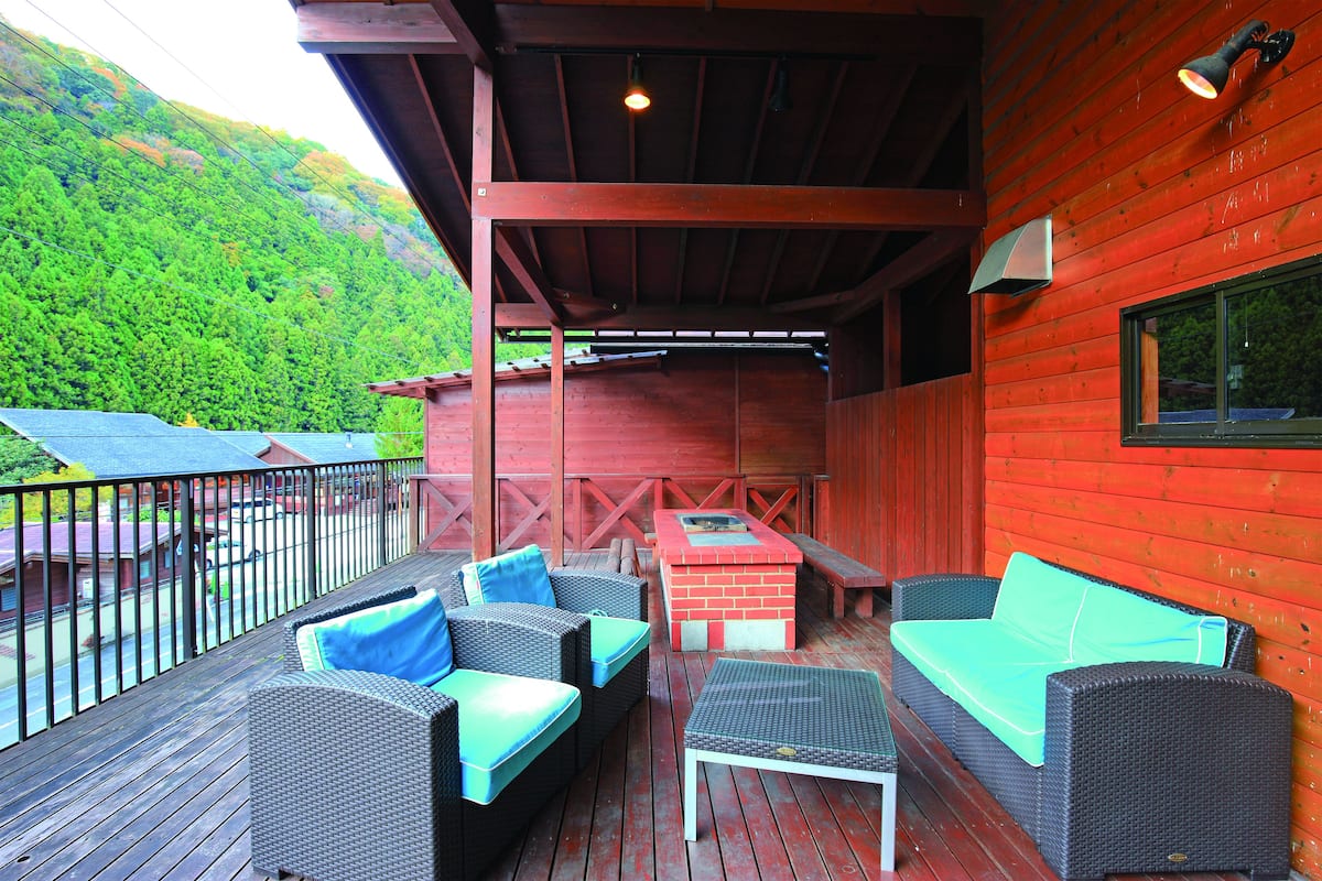 Eine Terrasse im Freien mit Korbmöbeln, einer Grillgelegenheit und Blick auf einen bewaldeten Hang.