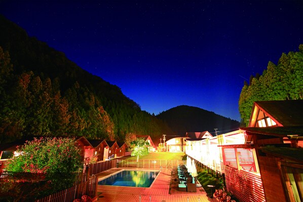 Ein Nachtblick auf einen Kurort mit Schwimmbad, Holzbungalows und einem Berg im Hintergrund.
