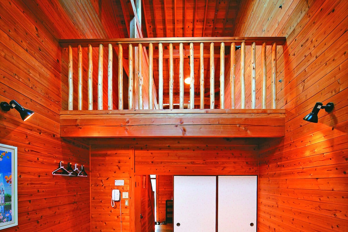 Ein Holzinnenraum mit Tatami-Boden, einer Holzbalkendecke und einem Balkon mit Geländer.