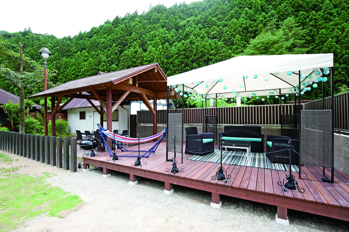 Eine Holzterrasse mit Gartenmöbeln, einer Hängematte und einem überdachten Sitzbereich mit Lichterkette.