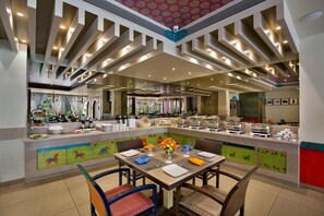A restaurant with a buffet setup, a dining area with tables and chairs, and a decorative ceiling.