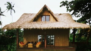 A thatched-roof hut with a wooden window, surrounded by lush greenery. - QI Palawan by Cocotel powered by ASTON (El Nido)