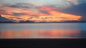 A sunset over a calm body of water with distant mountains. - QI Palawan by Cocotel powered by ASTON (El Nido)