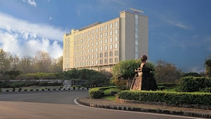 A hotel with a modern facade, a statue in the garden, and a well-maintained landscape. - Grand Keisha Yogyakarta (Depok)