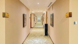 A hotel hallway with a carpeted floor, doors on either side, and numbered signs indicating room numbers. - Grand Keisha Yogyakarta (Depok)