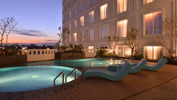 A hotel with a swimming pool, lounge chairs, and a well-lit building facade. - Grand Keisha Yogyakarta (Depok)