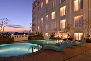 Un hotel con piscina, sillones de descanso y una fachada iluminada.