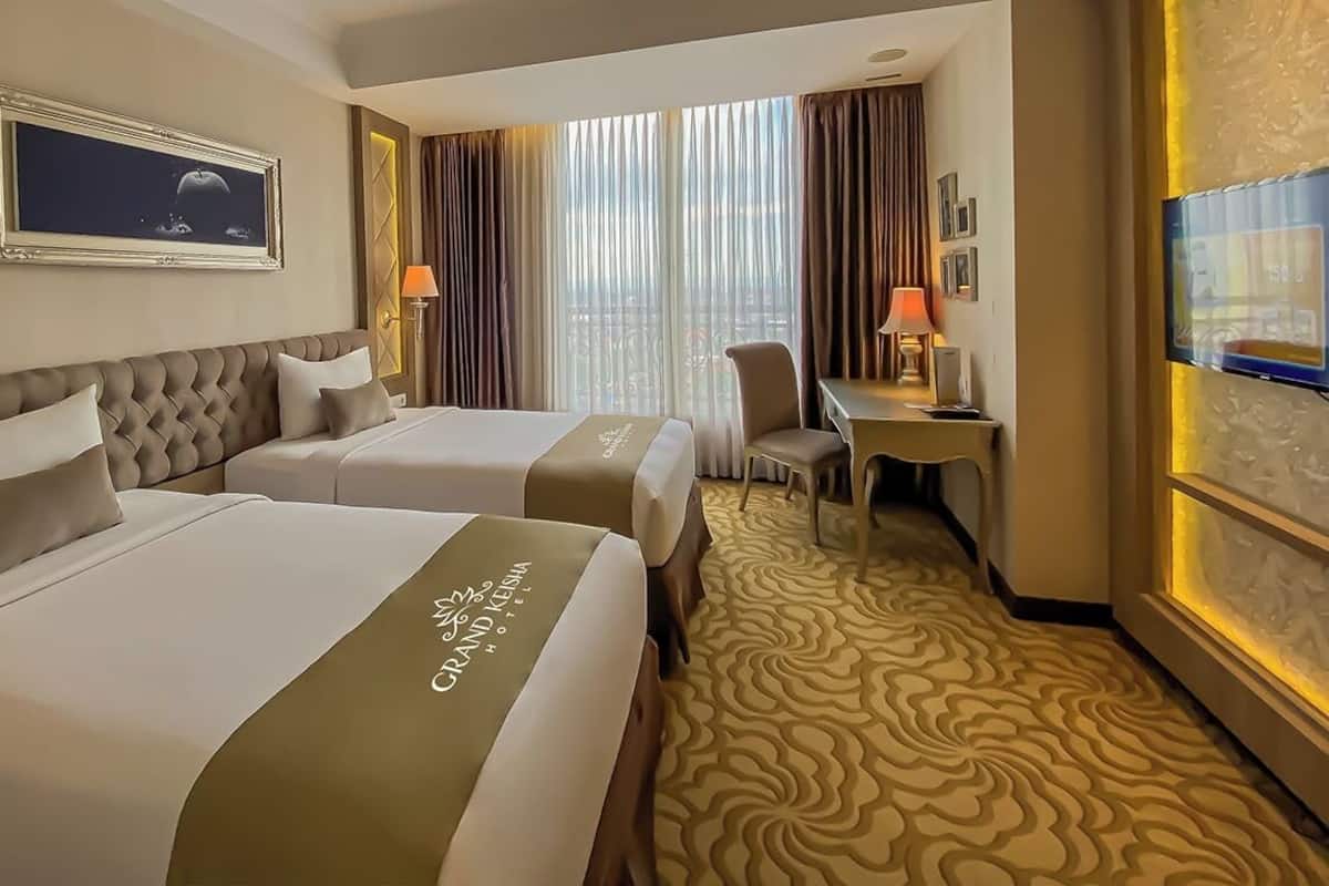 A hotel room with two beds, a desk, a chair, a television, and a large window with curtains.