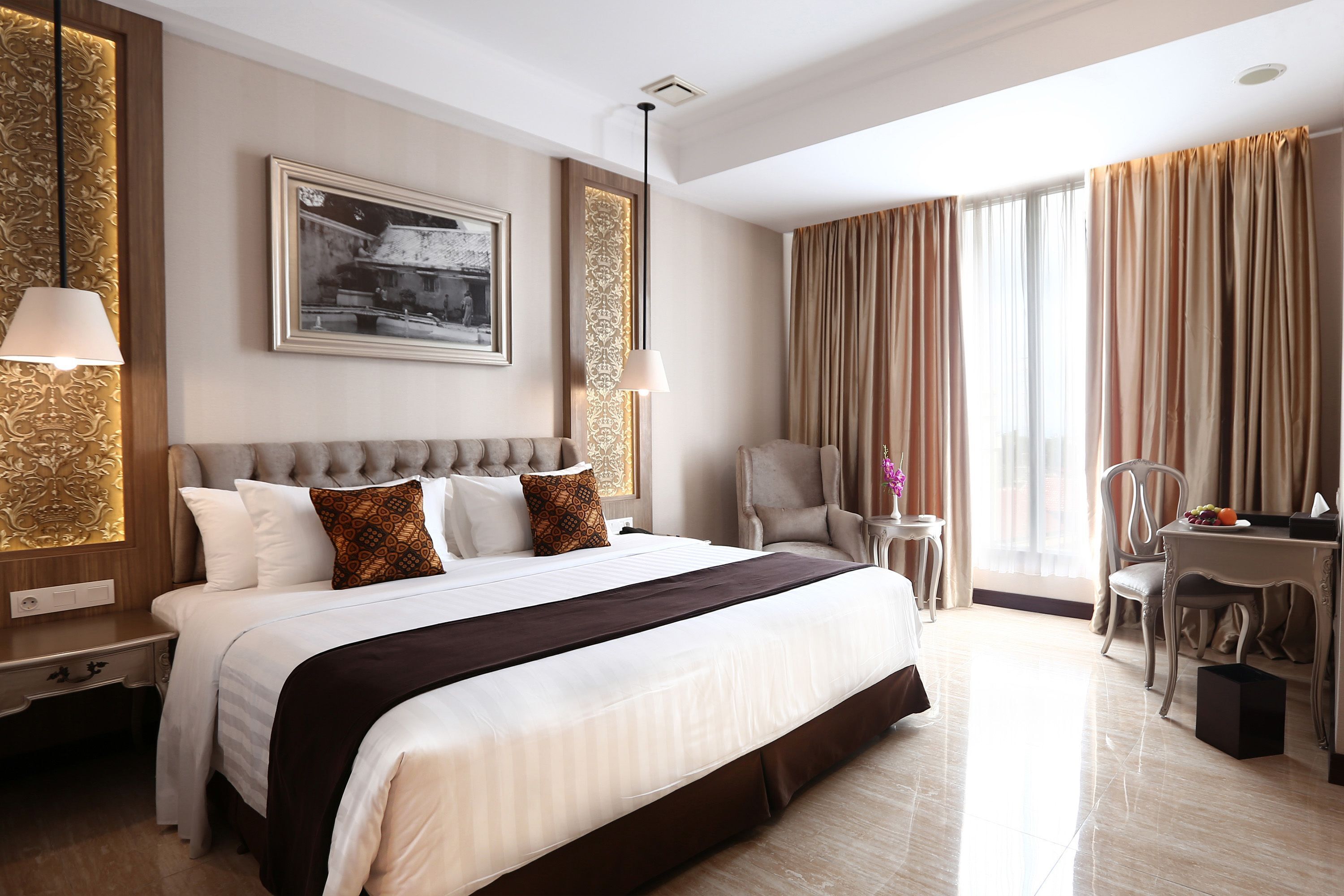 A hotel room with a large bed, a desk, a chair, a small table, and a window with curtains.