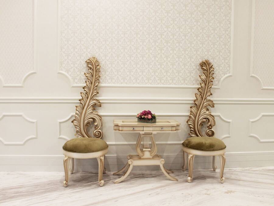 A room with two ornate chairs, a small table with a vase, and a patterned wall.