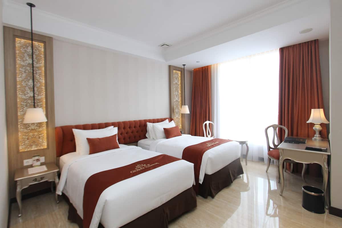 A hotel room with two beds, a desk, a chair, and a trash can.