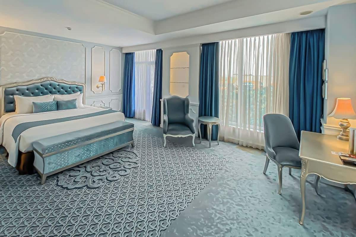 A hotel room with a large bed, a desk, a chair, and a small table.