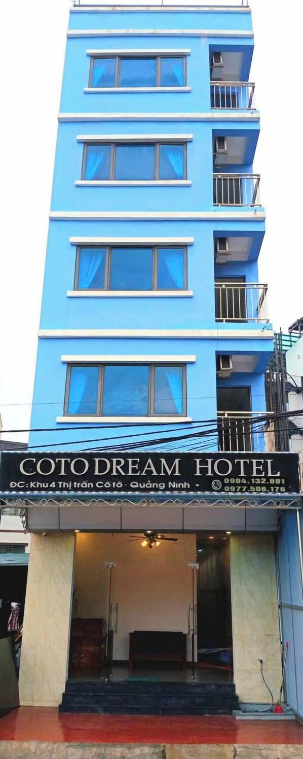 Un bâtiment bleu abritant un hôtel, avec une enseigne indiquant « COTODREAM HOTEL » et les coordonnées.
