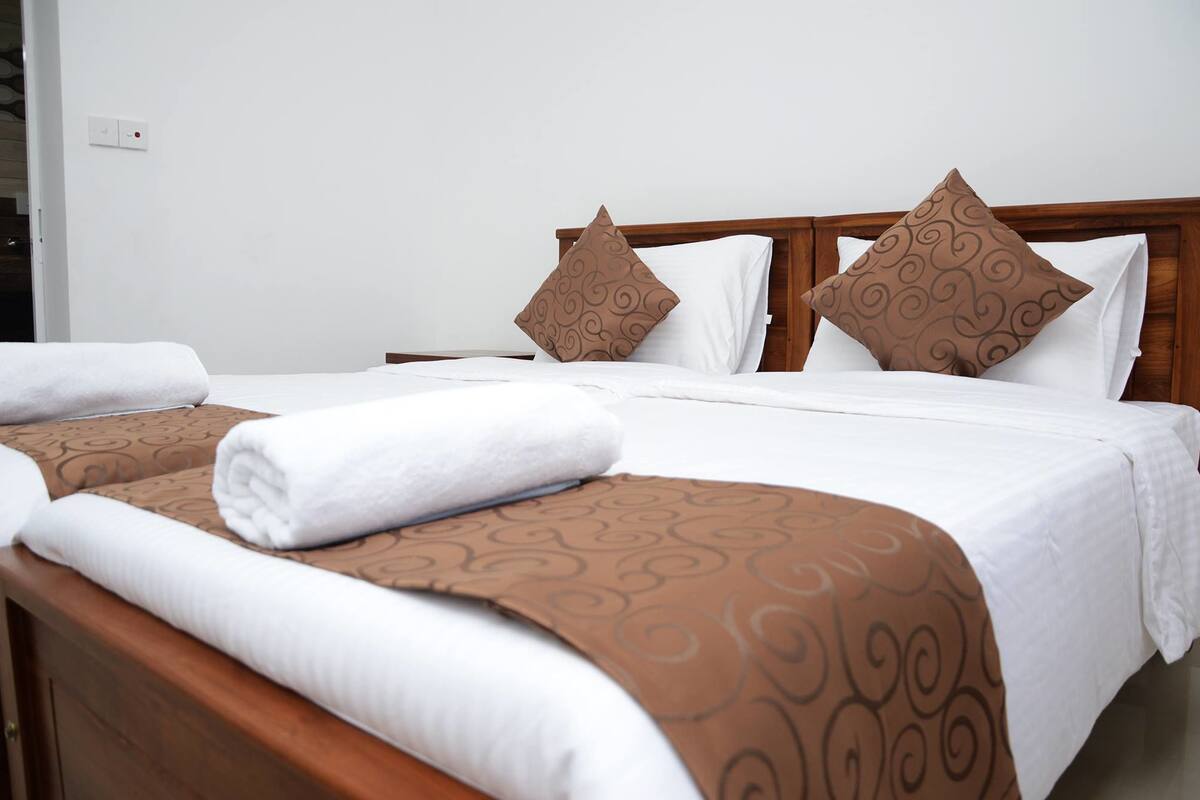Habitación de hotel con dos camas, cada una con una colcha marrón estampada y almohadas blancas.