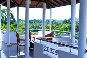 A covered outdoor area with white columns, wooden chairs, and a railing overlooking a lush green landscape. - Dazzling Villa (Kandy)