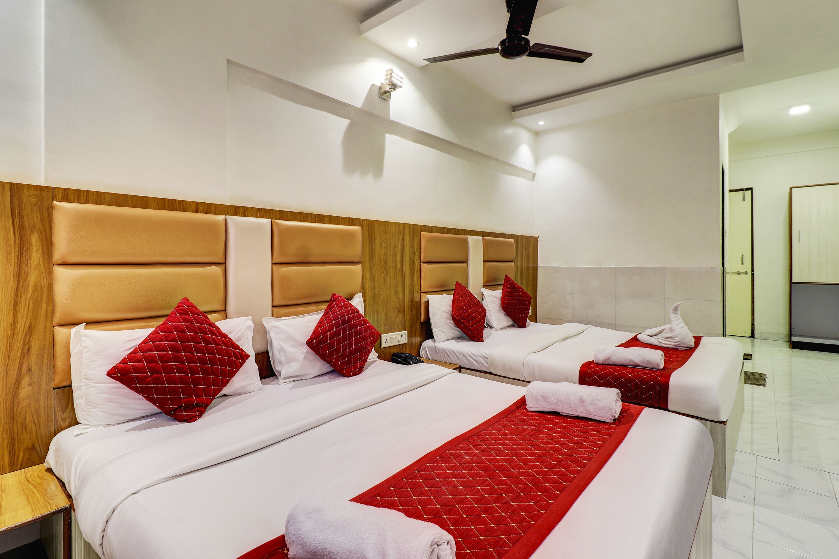 A hotel room with two beds, each with red and white bedding, wooden headboards, and red pillows.