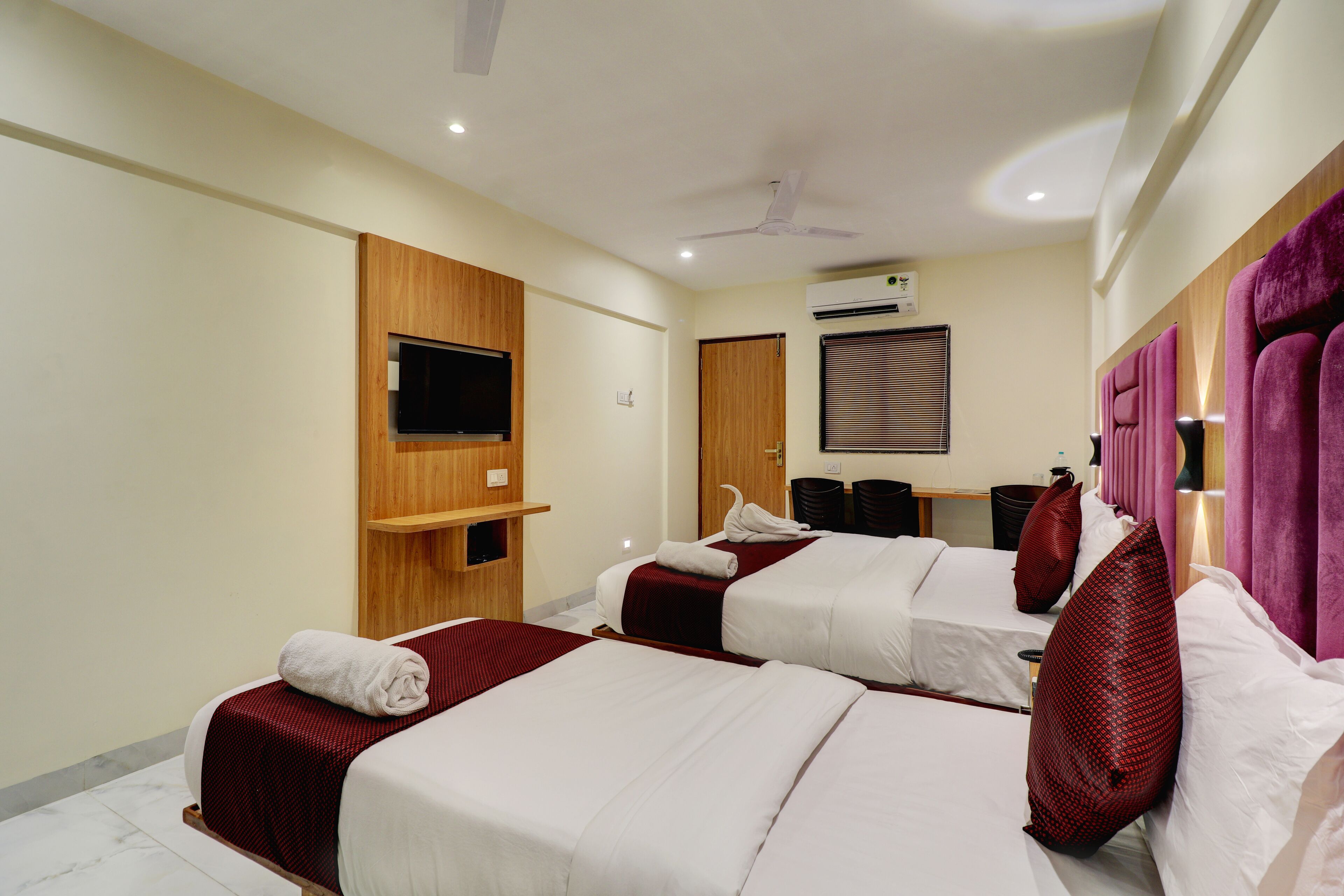 Habitación de hotel con dos camas, un televisor montado en la pared, un equipo de aire acondicionado y un ventilador de techo.