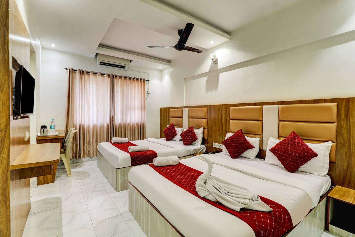 A hotel room with two beds, a desk, a television, and a shower area.