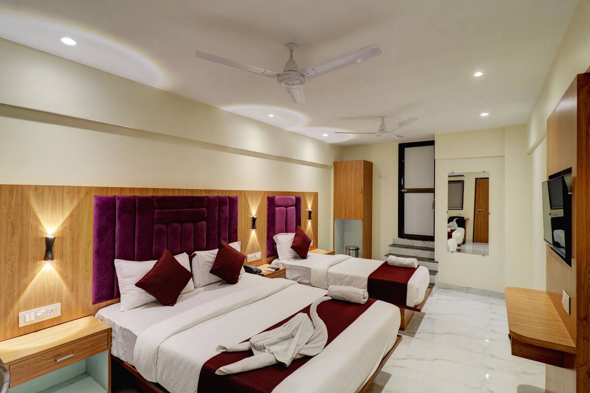 A hotel room with two beds, a TV, a ceiling fan, and a bathroom with a mirror and toilet.