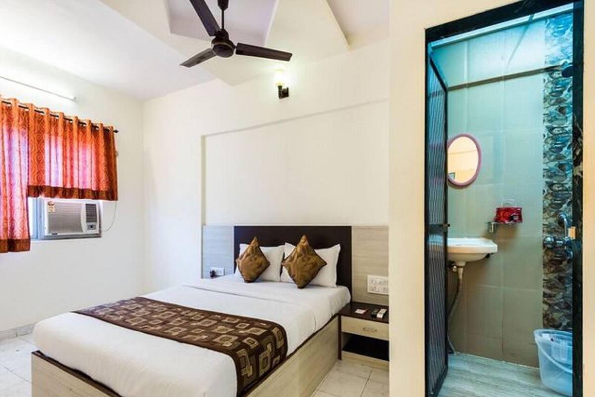 A hotel room with a bed, a nightstand, a ceiling fan, and a bathroom with a glass shower enclosure.