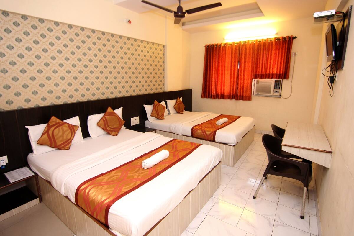 A hotel room with two beds, a desk, a chair, a ceiling fan, an air conditioning unit, and a patterned wall.