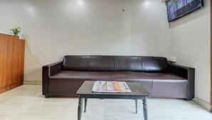 Un área de recepción con un sofá de cuero marrón, una mesita con una revista y un televisor de pared mostrando múltiples imágenes de cámaras.