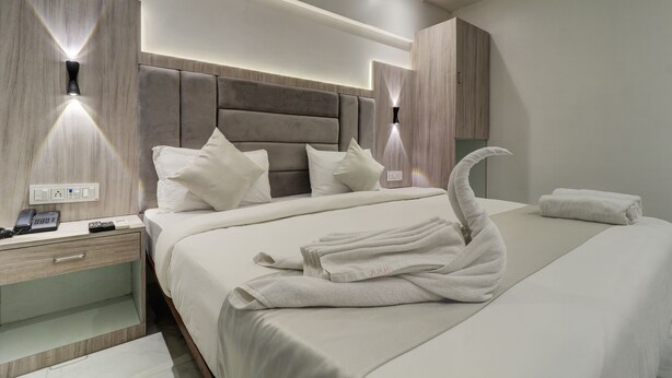 Una habitación de hotel moderna con una cama grande, una mesita de noche con un teléfono y controles remotos, y una cama bien hecha con una toalla dispuesta en forma de cisne.