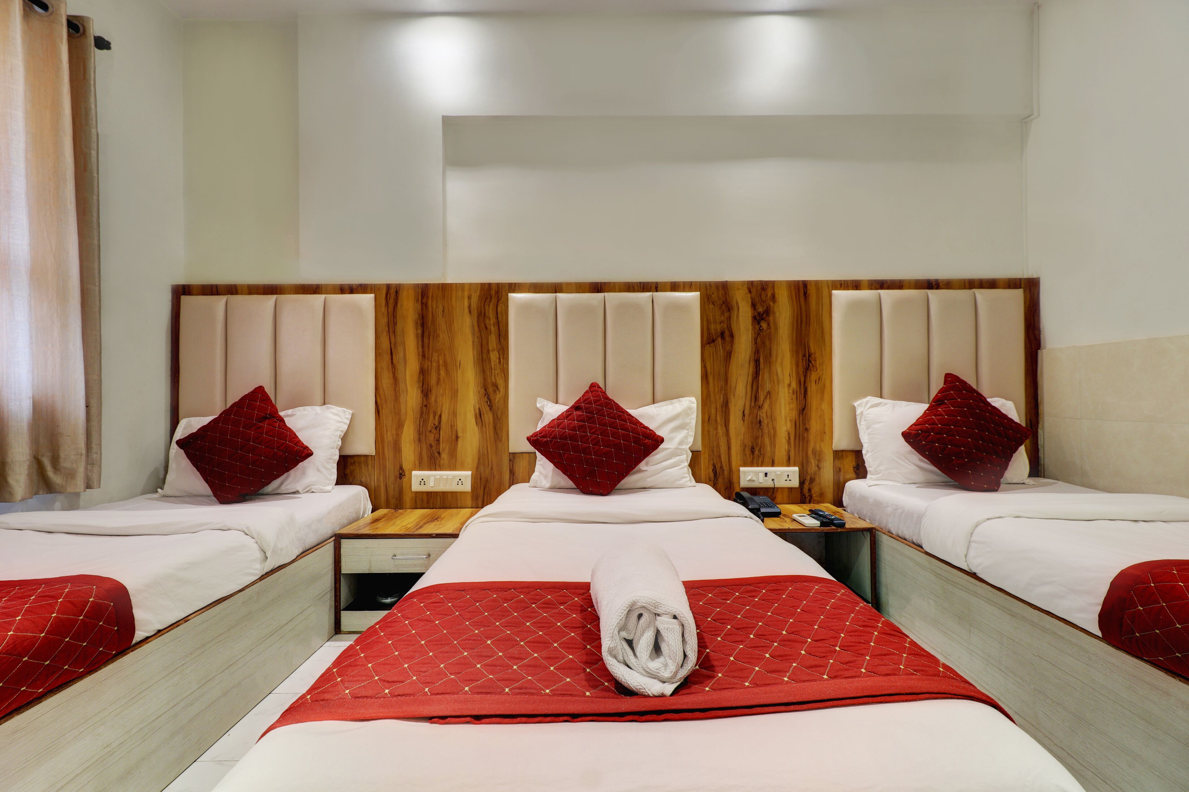 A hotel room with three beds, each with a red blanket and pillow, and a wooden headboard.