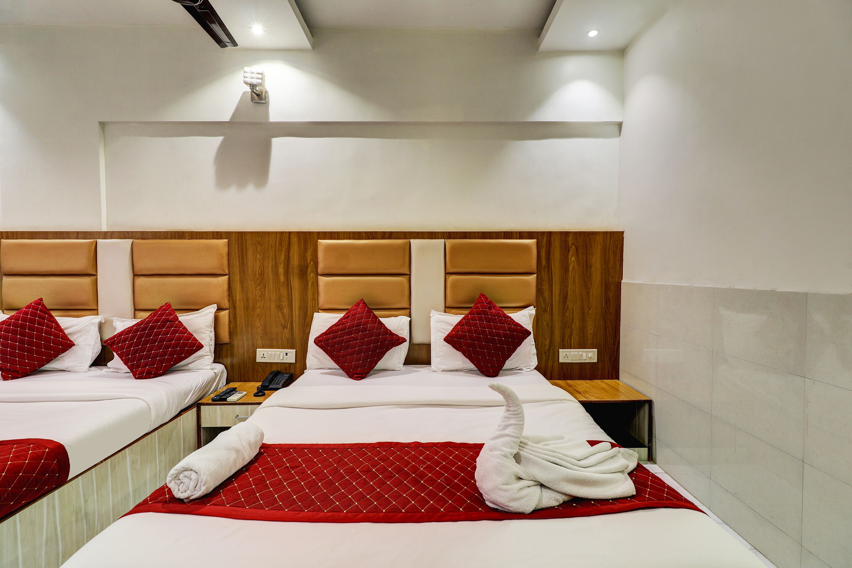 Une chambre d’hôtel avec deux lits, des oreillers rouges, une tête de lit en bois, une couverture rouge et une serviette sur le sol.