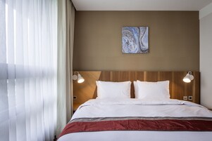 Een hotelkamer met een groot bed, twee bedlampjes, een kunstwerk aan de muur en transparante gordijnen.