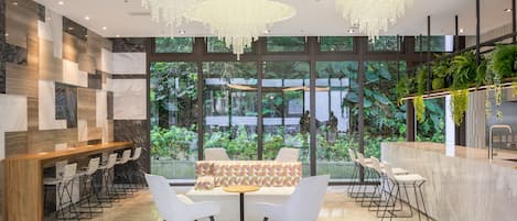 A modern lobby with a seating area, a reception desk, and large windows overlooking a garden.