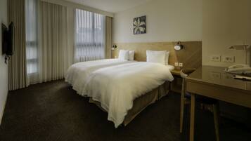 A hotel room with a large bed, a desk, a chair, a TV, and a window with curtains.